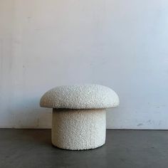 a large white stool sitting on top of a cement floor next to a white wall