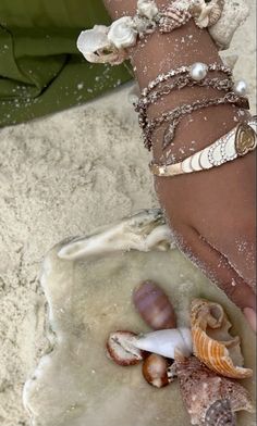 a woman's arm with shells and seashells on it, in the sand