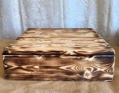 a wooden box sitting on top of a bed next to a window with curtains behind it