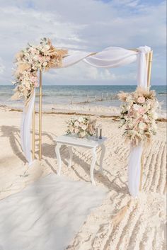 an outdoor wedding setup on the beach with white draping and floral arrangements in front of it