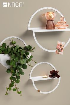 two white round shelves with plants and candles on them, next to each other in front of a gray wall