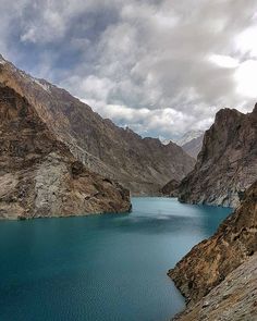 a large body of blue water surrounded by mountains and clouds in the distance with rocks on either side