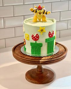 a decorated cake on a wooden stand in front of a white brick wall and tile backsplash