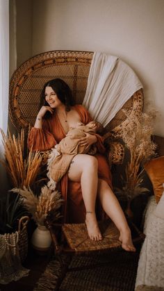 a woman sitting in a wicker chair next to a window with white drapes