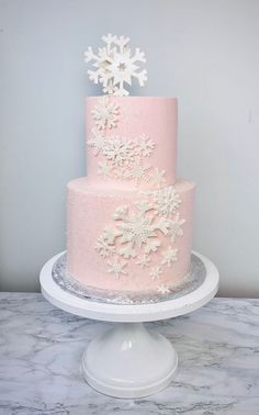 a pink and white cake with snowflakes on it sitting on top of a table