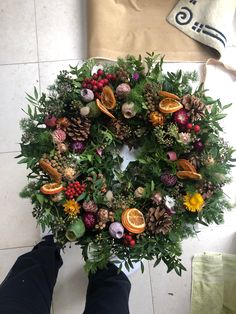 a person standing in front of a christmas wreath with fruit and leaves on it's side