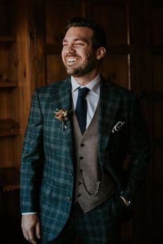 a man in a suit and tie smiles at the camera while standing next to a wooden wall