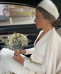 a woman sitting in the back seat of a car wearing a white dress and veil