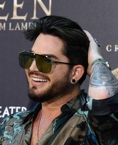 a man with tattoos and sunglasses holding his hair up to his head, smiling at the camera