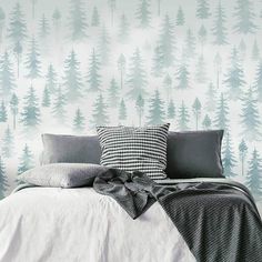 a bed with pillows and blankets in front of a forest wallpaper