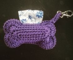 a purple crocheted dog bone shaped keychain with a white and blue flowered napkin on it