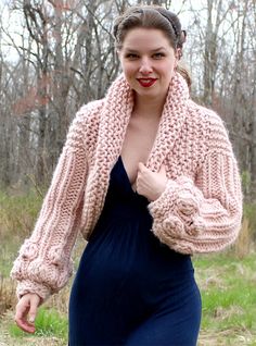 a woman in a blue dress and pink cardigan is walking through the woods with her hand on her hip