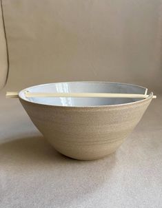 a white bowl with chopsticks in it on a beige surface next to a wall