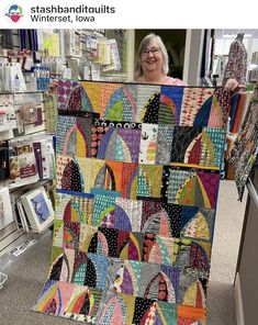 a woman holding up a colorful quilt in a store