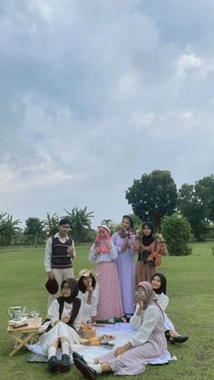 a group of people sitting on top of a grass covered field next to each other