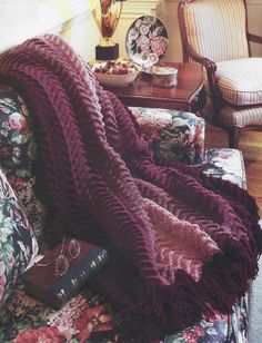 a purple blanket is draped over a floral couch with a book on the end table