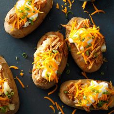 four loaded baked potatoes with shredded cheese and green onions on top, sitting on a black surface