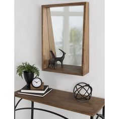 a wooden mirror hanging on the wall above a table with a clock, plant and other items