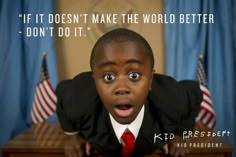 a young boy wearing a suit and red tie with an american flag behind him in front of a desk