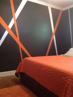 a bed with an orange bedspread sitting in front of a black and white wall