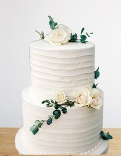 a white wedding cake with flowers and greenery on the top is sitting on a wooden table