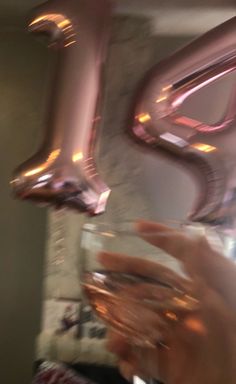 a person holding a wine glass in front of some foil balloons that are shaped like the letter e