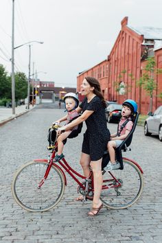 a woman riding a bike with two children in the front and one on the back