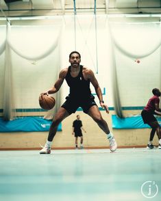 a man holding a basketball while standing on top of a basketball court with other people around him