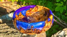 a blue glass bowl sitting on top of a wooden stand in front of some trees