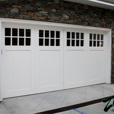 a white garage door with windows in front of a stone wall and black shutters