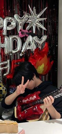 a man sitting at a table with a guitar in front of him and balloons behind him