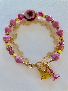 Lovely double strand beaded Premium Czech glass flower bracelet featuring Picasso pink turbine beads, Czech pink sea glass, pink cherub fire polished crystals, and single 15 mm pink Picasso pansy flower. All accented with antique gold plated daisies and shiny cubes. Satin Hamilton rose chain adds the perfect delicate second strand. Premium gold electroplated brass chain in satin finish with intricate rose flower pattern. Bracelet is beaded on professional Soft Flex beading wire with high quality Adjustable Pink Single Strand Beaded Bracelets, Adjustable Pink Single Strand Beaded Bracelet, Adjustable Single Strand Pink Beaded Bracelet, Adjustable Pink Charm Bracelet With Spacer Beads, Pink Beaded Czech Glass Jewelry, Pink Glass Jewelry With Colorful Beads, Pink Glass Jewelry With Faceted Beads, Pink Glass Beaded Bracelets As Gift, Adjustable Pink Glass Bracelets