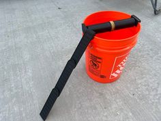 an orange bucket sitting on the ground with a black stick sticking out of it's side