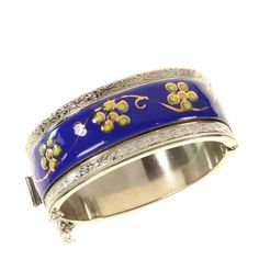 Vintage Wide Hinged Bangle Blue Enamel Floral Silver Tone Here's an interesting wide hinged bangle bracelet with an applied front section of royal blue enameled metal with hand painted flowers and gold leaf. The bracelet has an embossed and milgrain top and bottom border design.  Push-in clasp with safety chain.  No maker hallmarks found.    Condition: Previously owned, good vintage condition with no noted damage.  The hinge, push-in clasp, and safety chain all hold securely. Measures Approximately: Interior Measurements for Fit 2-3/8 x 2-1/16 in.  Bracelet Width is 1 in. Thank you for visiting Clara's Chic Boutique! More vintage jewelry: https://www.etsy.com/shop/ClarasChicBoutique?ref=seller-platform-mcna0v§ion_id=13953588 More items at Clara'sChicBoutique:  claraschicboutique.etsy.com Interior Measurements, Vintage Bangles, Safety Chain, Hand Painted Flowers, Painted Flowers, Hinged Bangle, Vintage Bracelets, Border Design, Chic Boutique