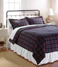 a bed with a plaid comforter and pillows on it in a room next to a window