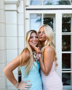 two beautiful women standing next to each other in front of a white building with windows