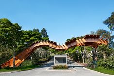 a curved wooden walkway in the middle of a park with trees and bushes around it