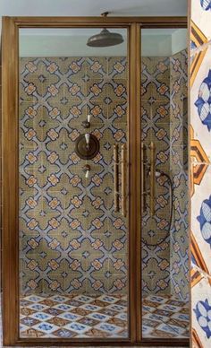 an ornate tiled shower with glass doors and tile flooring in a bathroom area that has blue and orange tiles on the walls