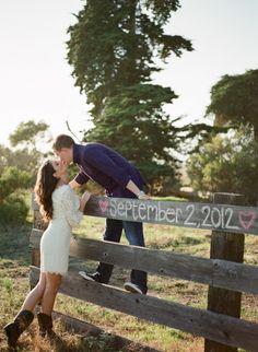 a man kissing a woman on the cheek in front of a fence with words written on it