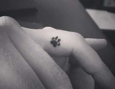 a person with a small paw tattoo on their finger and the other hand is holding an animal's paw