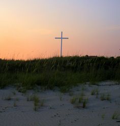 a cross on top of a hill in the middle of grass and sand at sunset