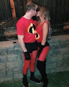 a man and woman dressed up as the incredibles kissing in front of a brick wall