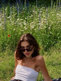 a woman sitting in the grass with sunglasses on her face and flowers in the background