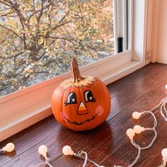 a pumpkin sitting on top of a wooden floor next to a window with string lights