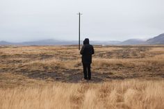 a person standing in the middle of an open field with tall grass and mountains in the background