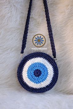 a blue and white crocheted purse with an evil eye on the front hanging from a chain