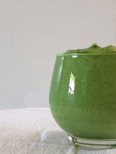 a green drink in a glass on top of a white table cloth with a spoon next to it