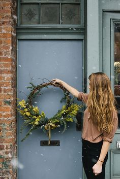 a woman is standing in front of a blue door with a wreath on the side