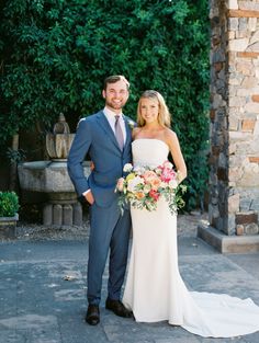 a bride and groom pose for a photo in front of an archway with greenery