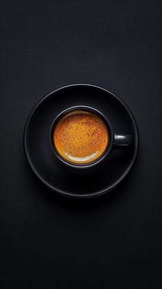 a black plate topped with a cup of coffee on top of a dark countertop